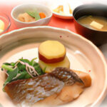 焼き魚と野菜が盛られた定食。食堂での食事風景。